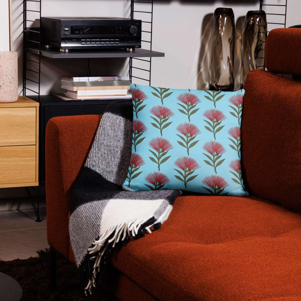 Pohutukawa print cushion with sky blue background sitting on a red velour sofa