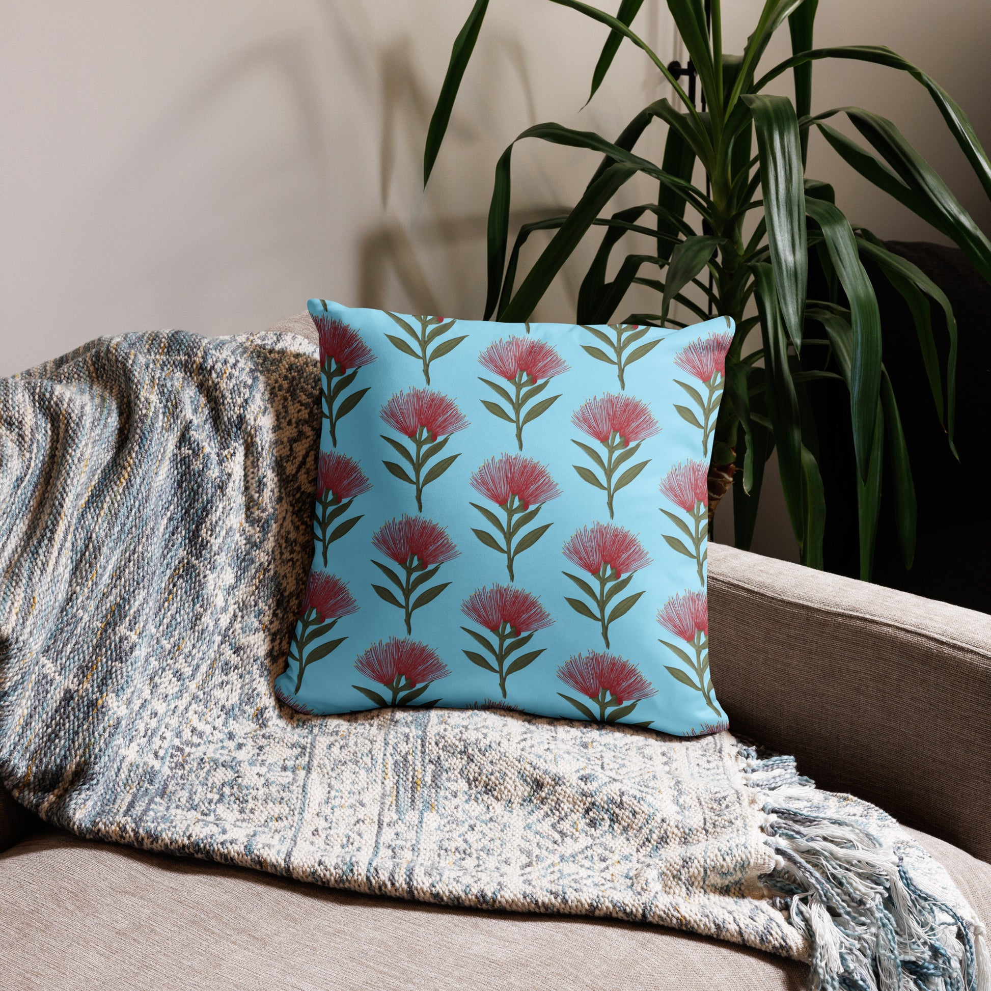 Pohutukawa print cushion with sky blue background sitting on a beige sofa with a plant behind it