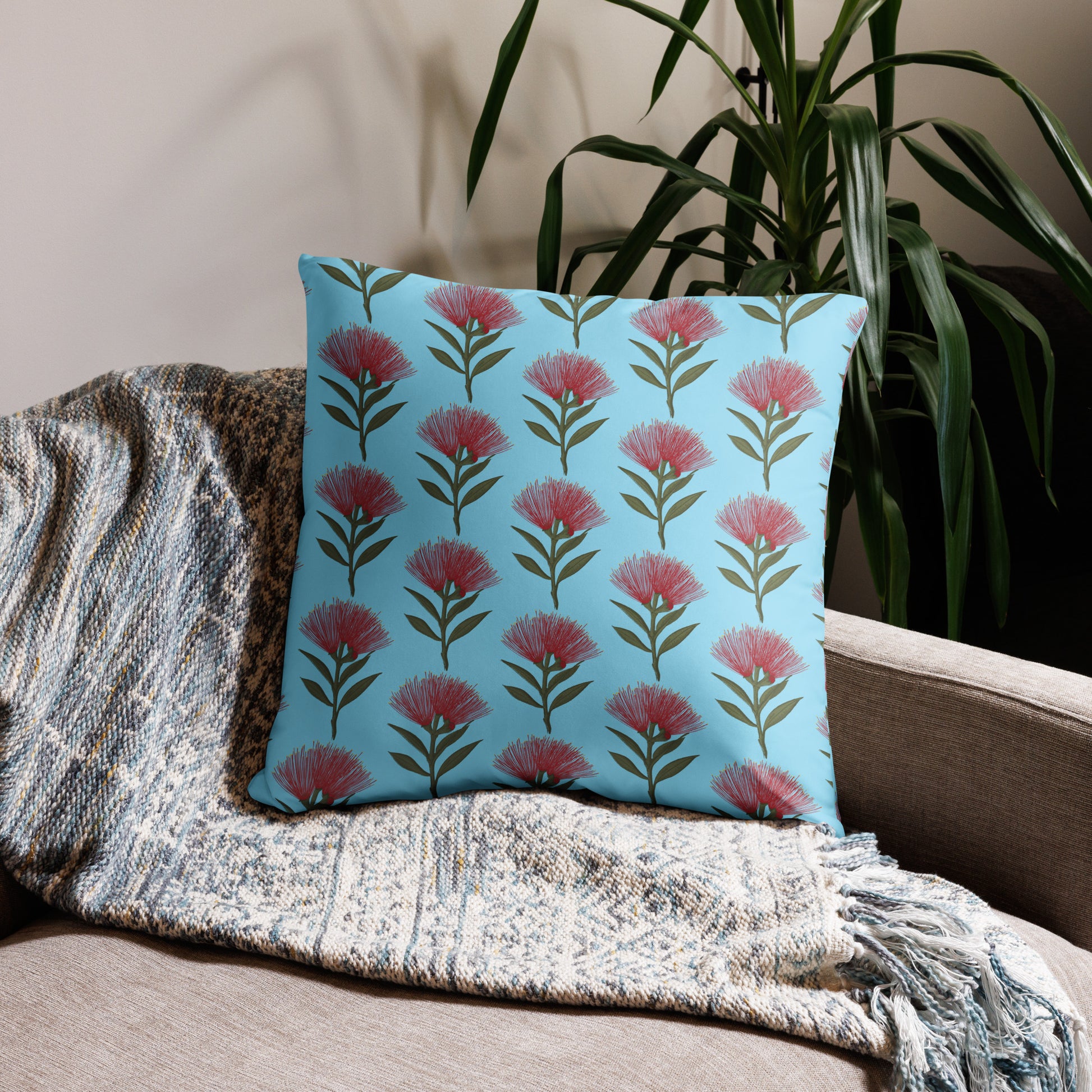 Pohutukawa print cushion with sky blue background sitting on a beige sofa with a plant behind it