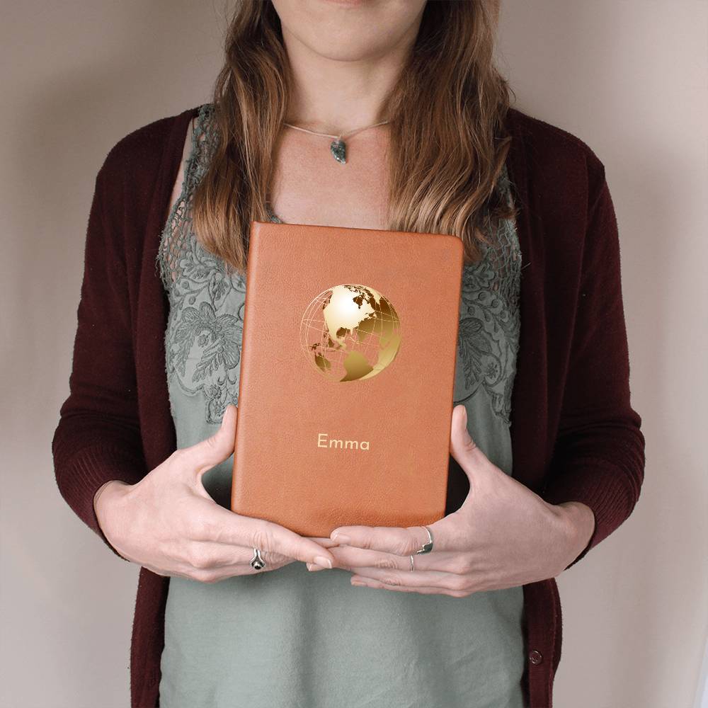 Woman holding tan vegan leather travel journal. It has a golden globe graphic and a personalised name 'Emma'