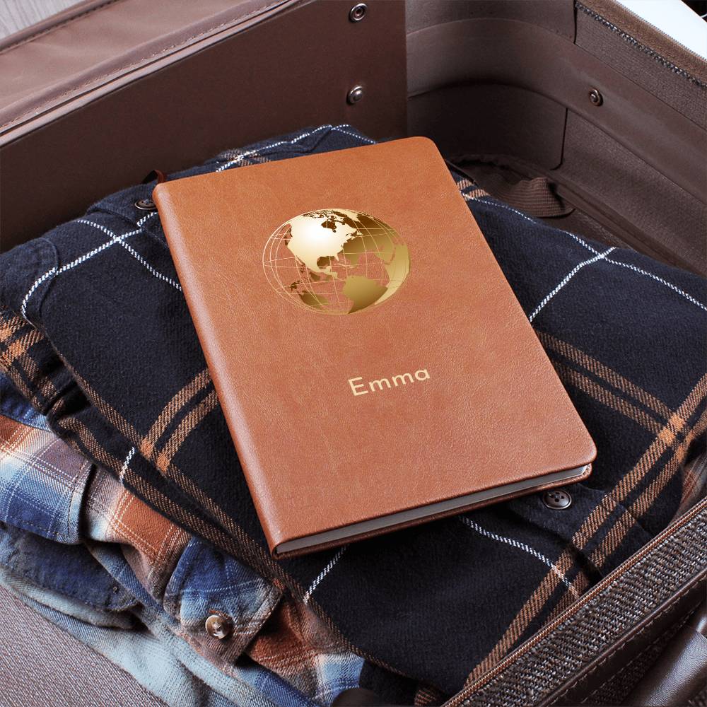 Photo of front of tan vegan leather travel journal. It has a golden globe graphic and a personalised name 'Emma'. Pictured lying on top of a tartan folded travel rug.